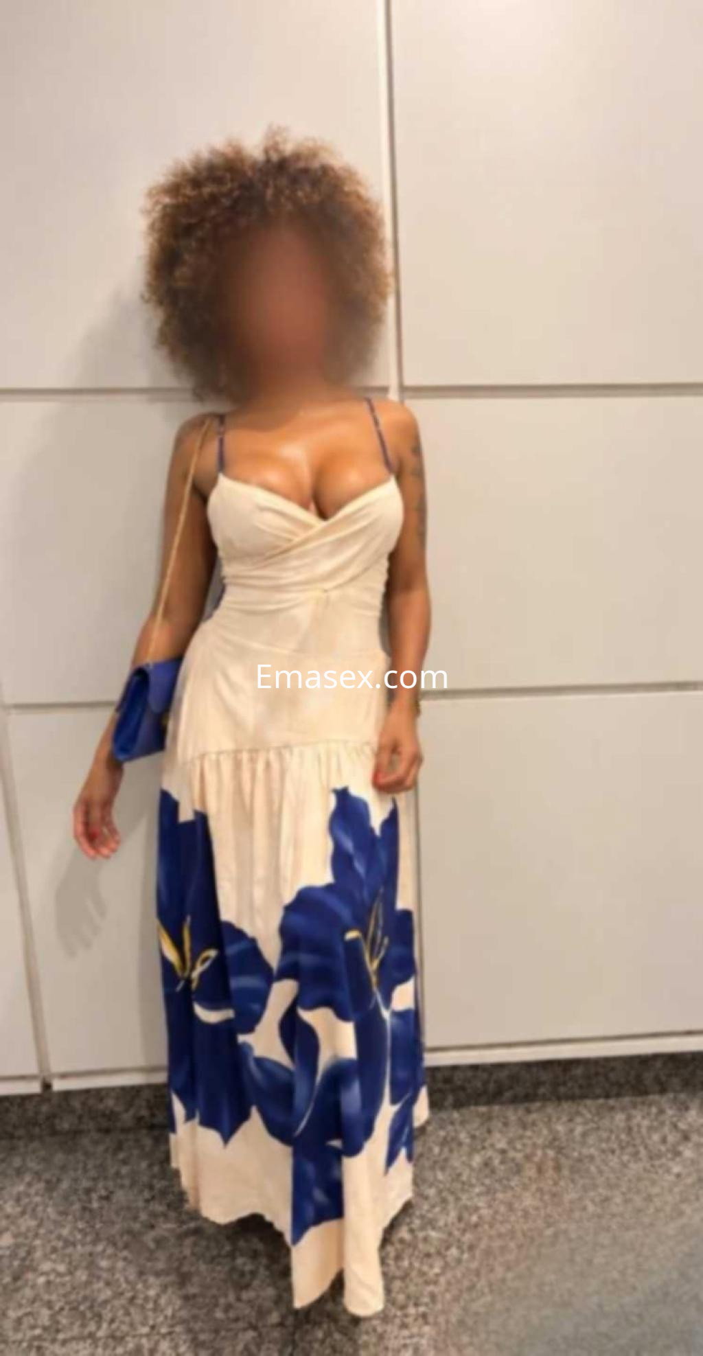 Escort en Valladolid con cabello rizado y suelto, luciendo un vestido largo de flores y posando en un entorno moderno.