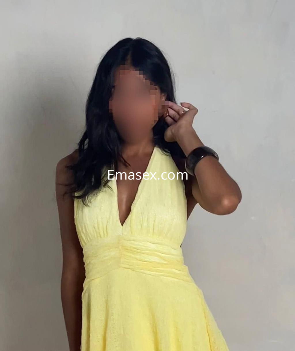 La escort en Alicante lleva un vestido amarillo con escote, posando de manera elegante y casual.