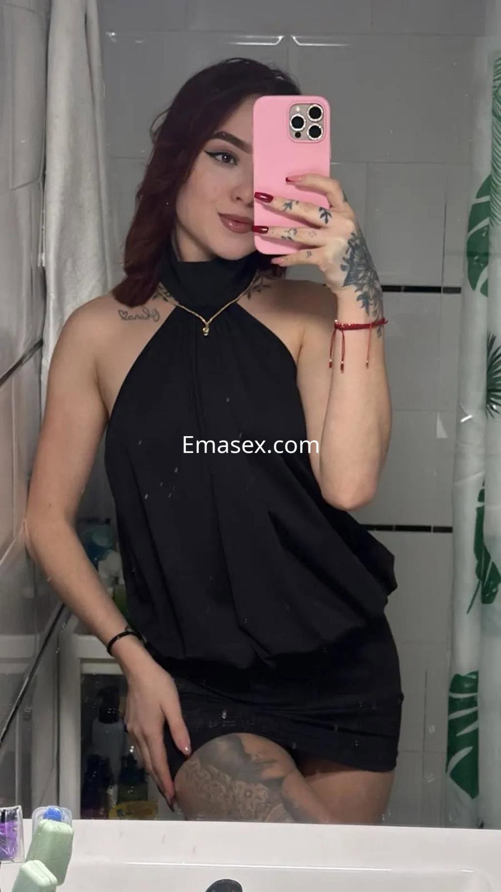 Puta en Alicante con vestido negro sin mangas, posando en un baño con un espejo y detalles decorativos verdes.