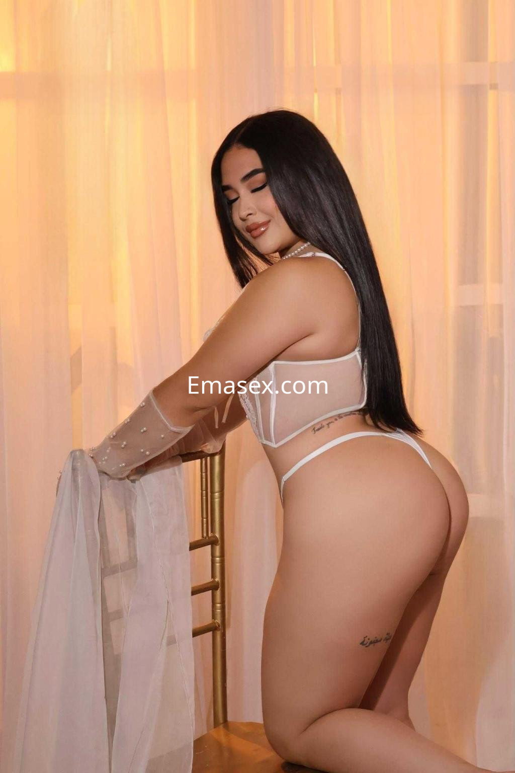 Puta en Murcia posando de espaldas con lencería blanca y una ligera transparencia, cabello largo y lacio.