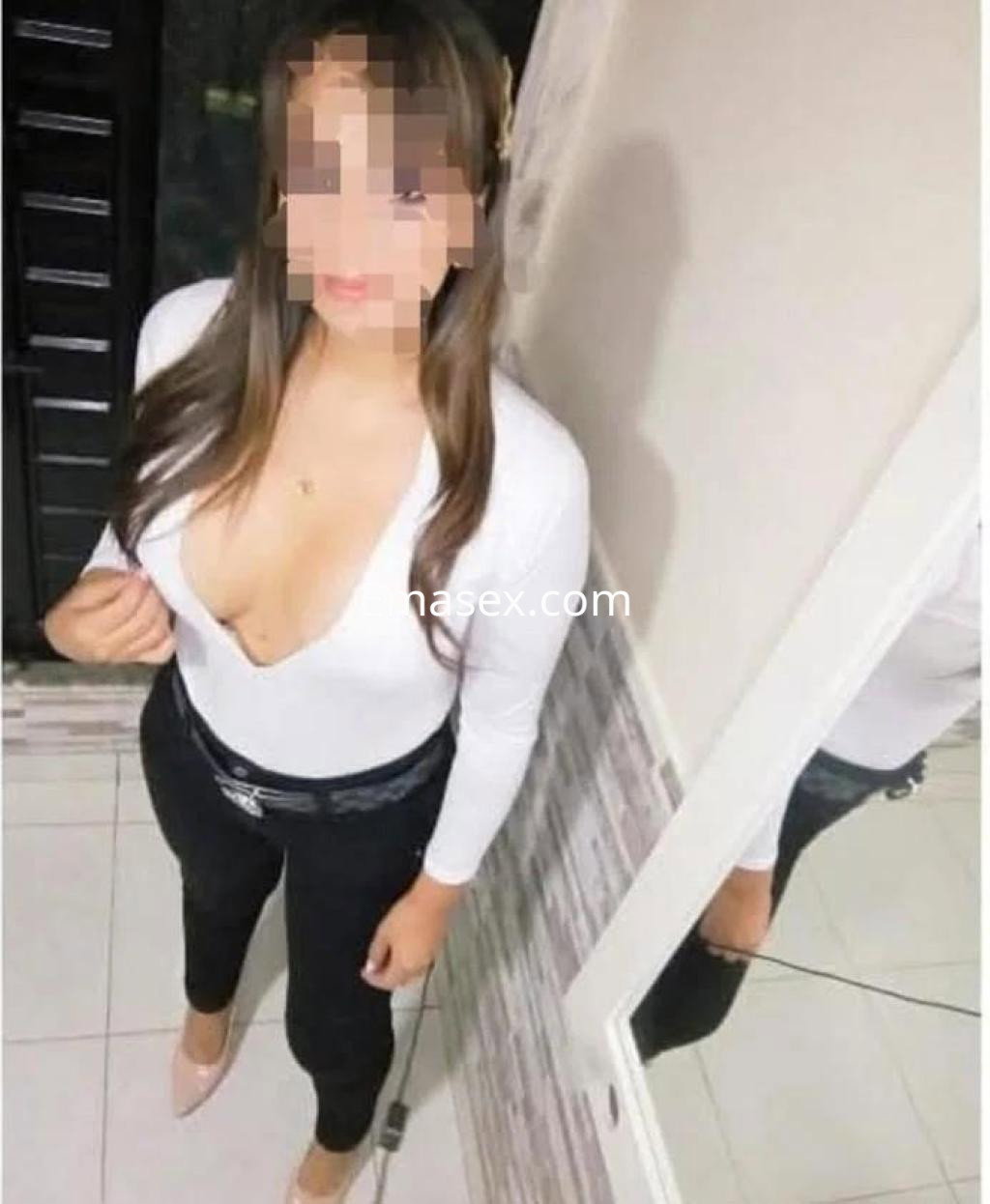 Escort en Las Palmas con blusa blanca de escote y pantalones negros ajustados, posando frente a un espejo.