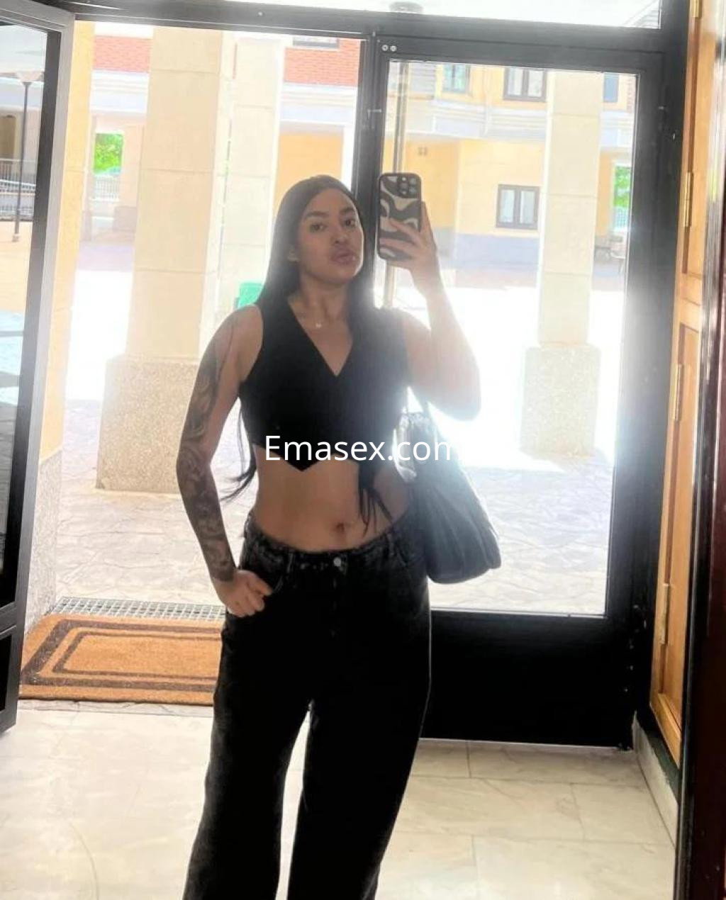 Puta en Zamora, posando frente a un espejo con top negro y pantalones anchos, mostrando un look casual.