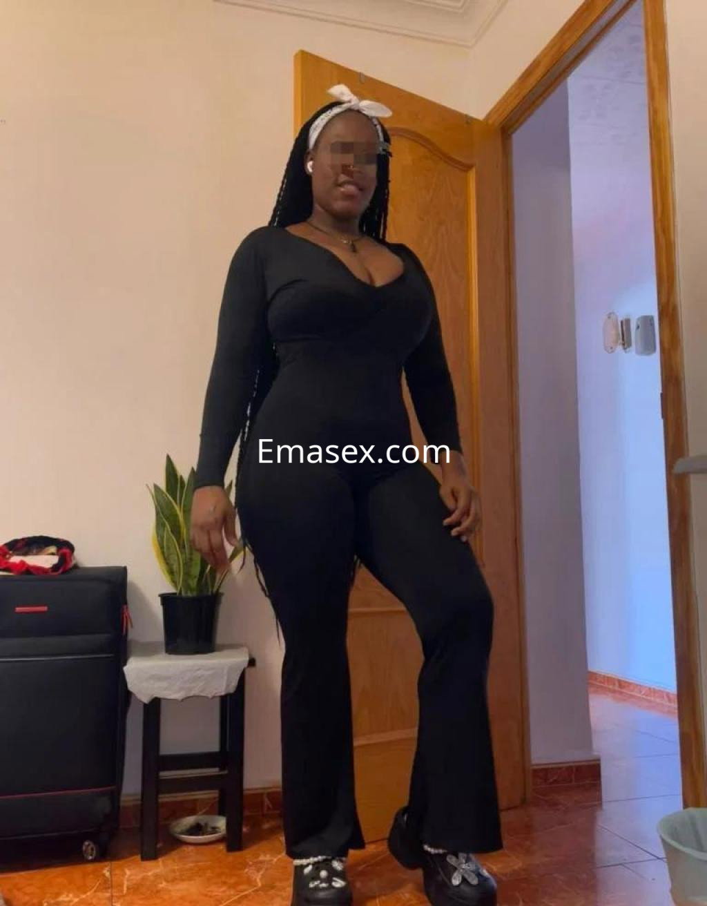 Escort de Zamora posando en un ajustado mono negro con cabello trenzado y un lazo en la cabeza.