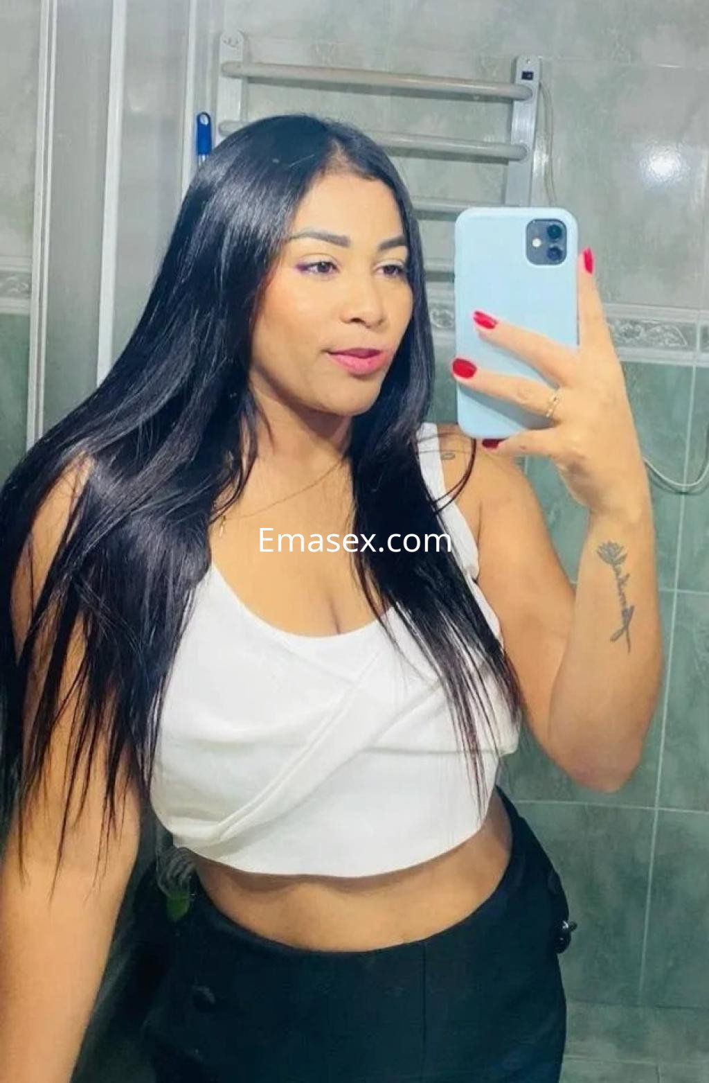 Puta en Valladolid, posando en un baño con un top blanco y cabello largo, sonriendo mientras se toma una selfie.