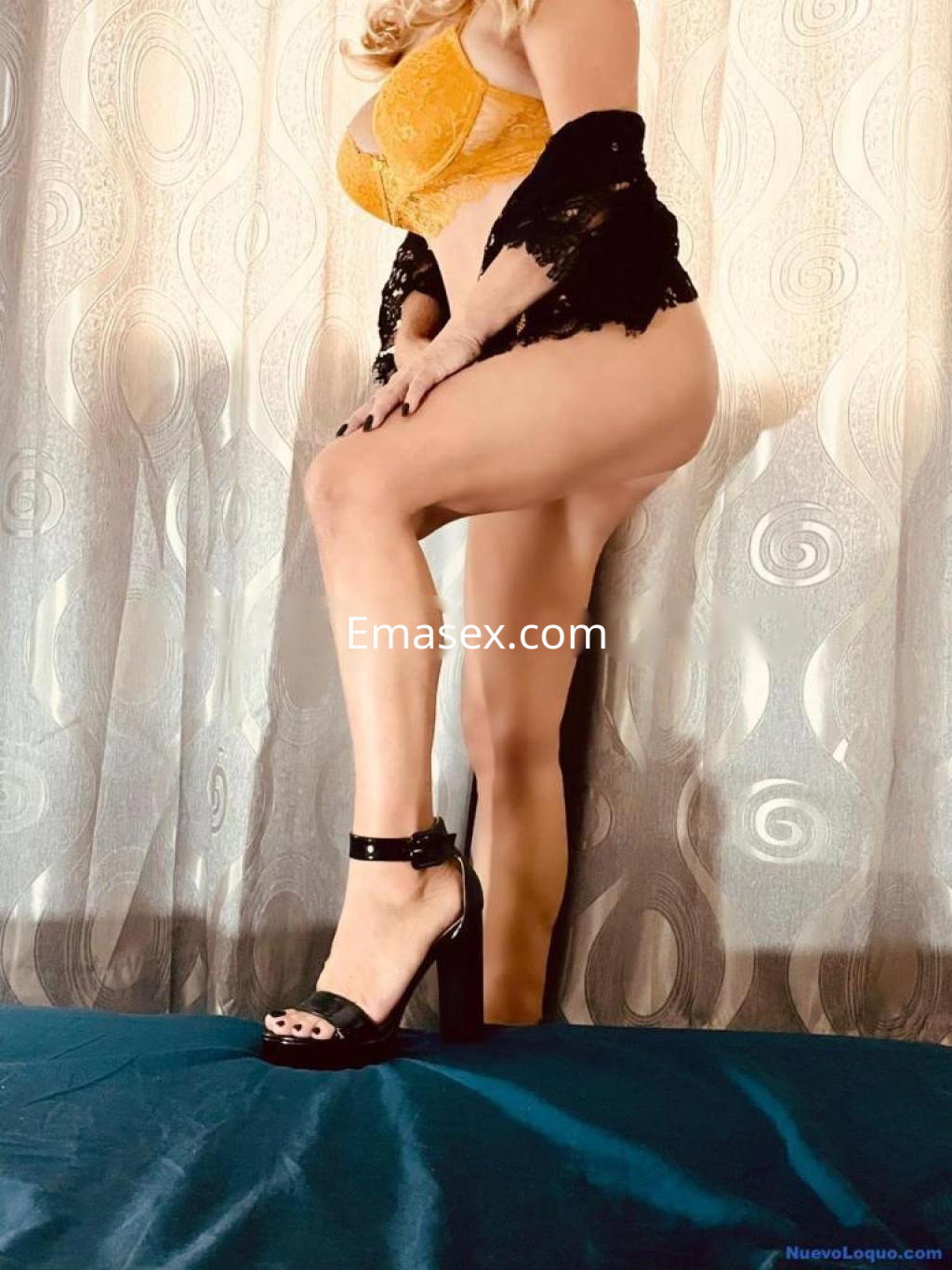 Puta en Girona con lencería amarilla y chal negro, posando de perfil con una pierna levantada y tacones.
