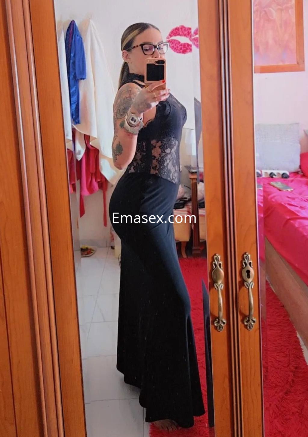 Puta en Córdoba, luciendo un vestido negro ajustado con encaje, posando frente a un espejo en un ambiente acogedor.