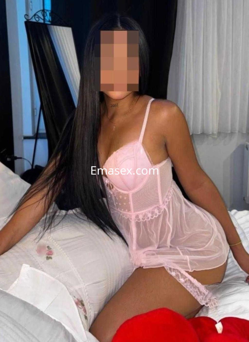 Puta en Madrid, viste una babydoll rosa transparente y se encuentra recostada sobre la cama con el cabello largo.