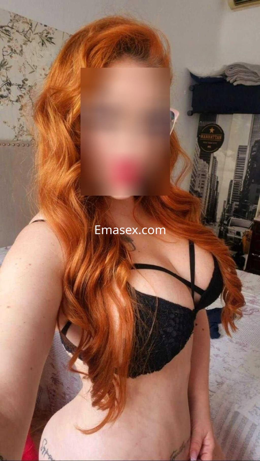 Escort con cabello largo y rizado de color naranja, vistiendo un sujetador negro en un entorno interior en Murcia.