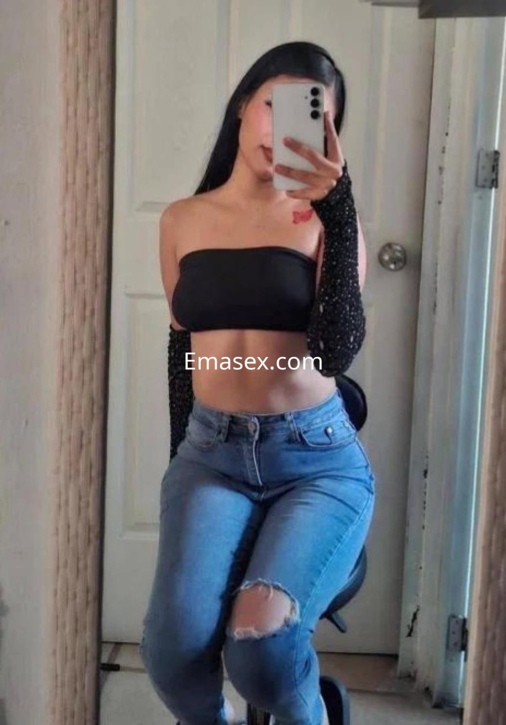 Puta se toma una selfie en Madrid, luciendo un top negro sin mangas y guantes largos, con jeans ajustados y un fondo neutro.