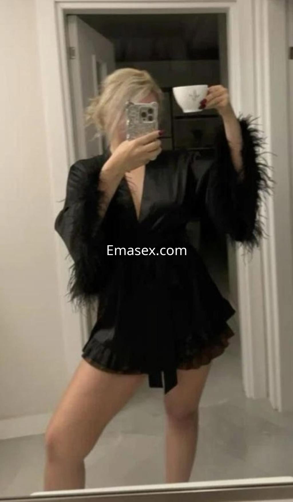 Puta en Las Palmas se toma una selfie en un espejo, vistiendo un kimono negro con plumas y una falda corta.