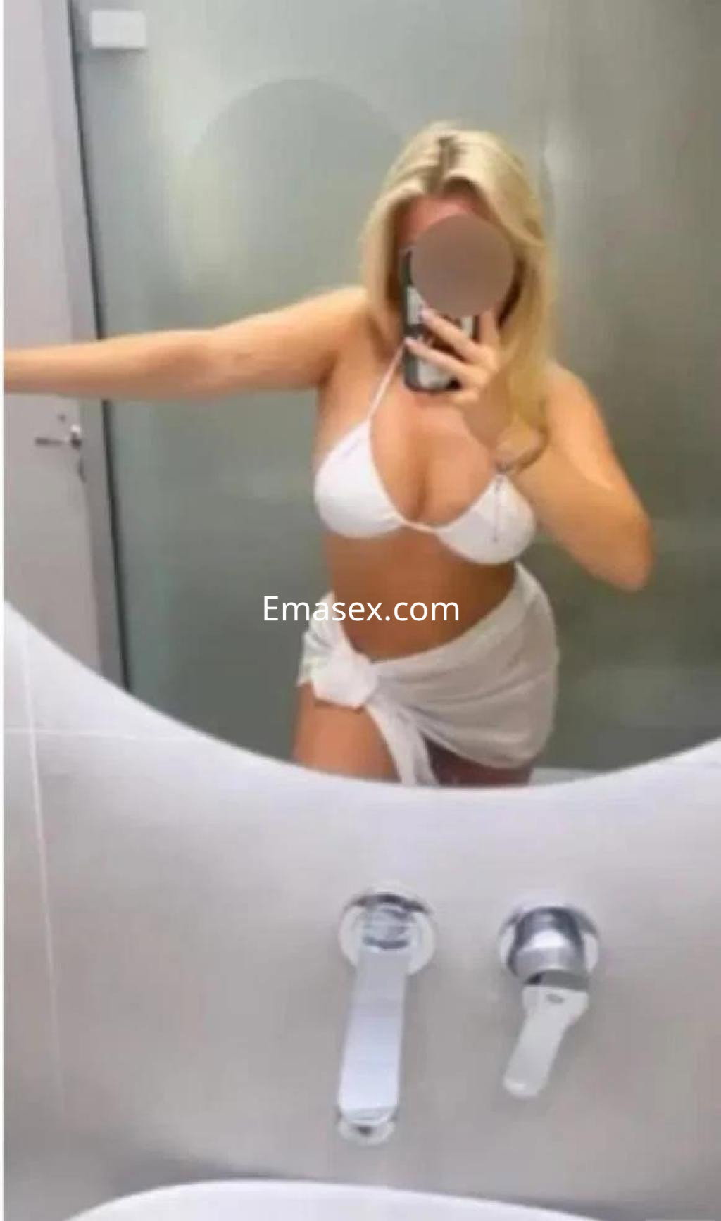 Escort en Badajoz con cabello rubio, usando un conjunto blanco mientras se mira en un espejo.