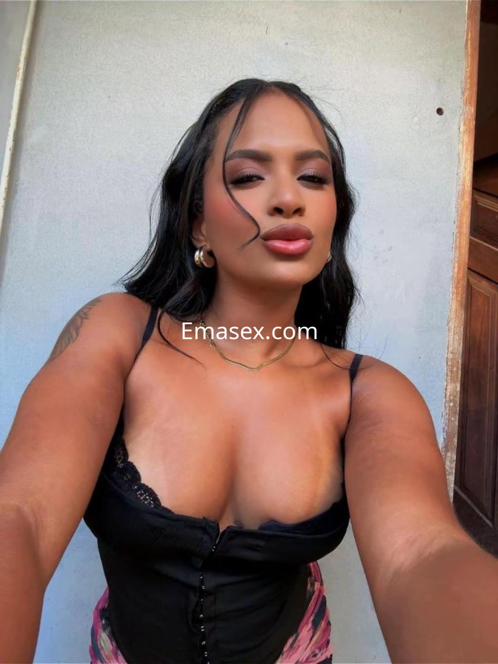 Escort en Donosti con cabello oscuro, blusa negra ajustada y un fondo neutro, posa con confianza.