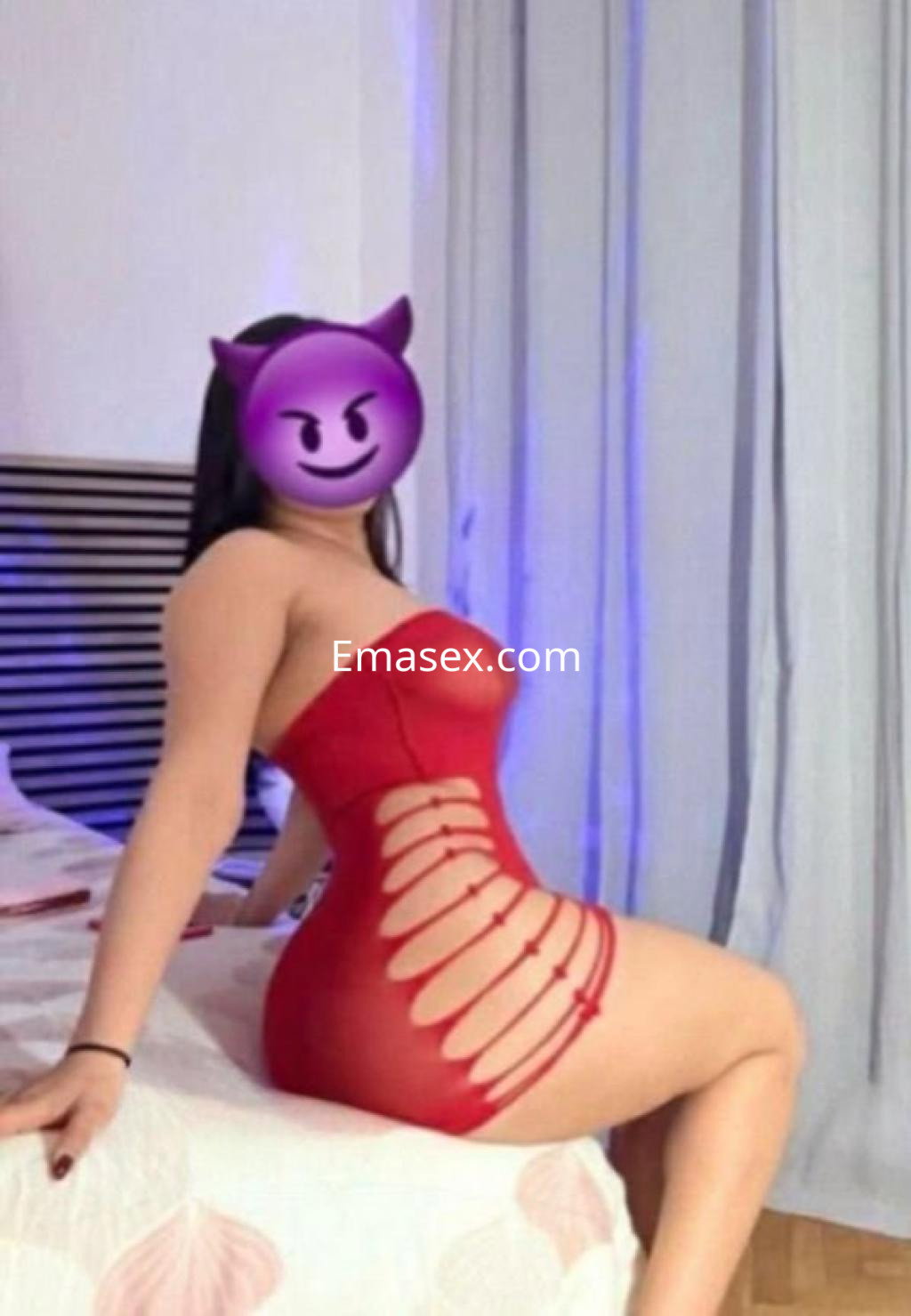 La puta en Tarragona posa sobre una cama con sábanas claras, luciendo un vestido rojo ajustado y sugerente.