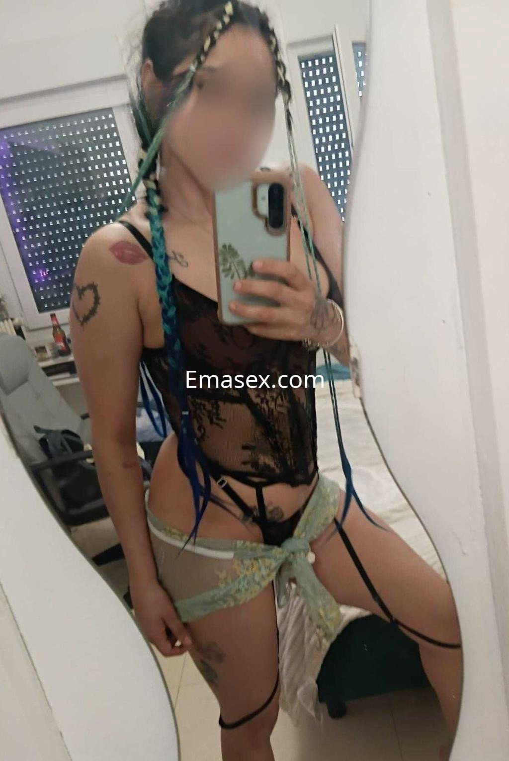 Puta en Córdoba frente al espejo, luciendo un body transparente con detalles en encaje y cintas que acentúan su figura.