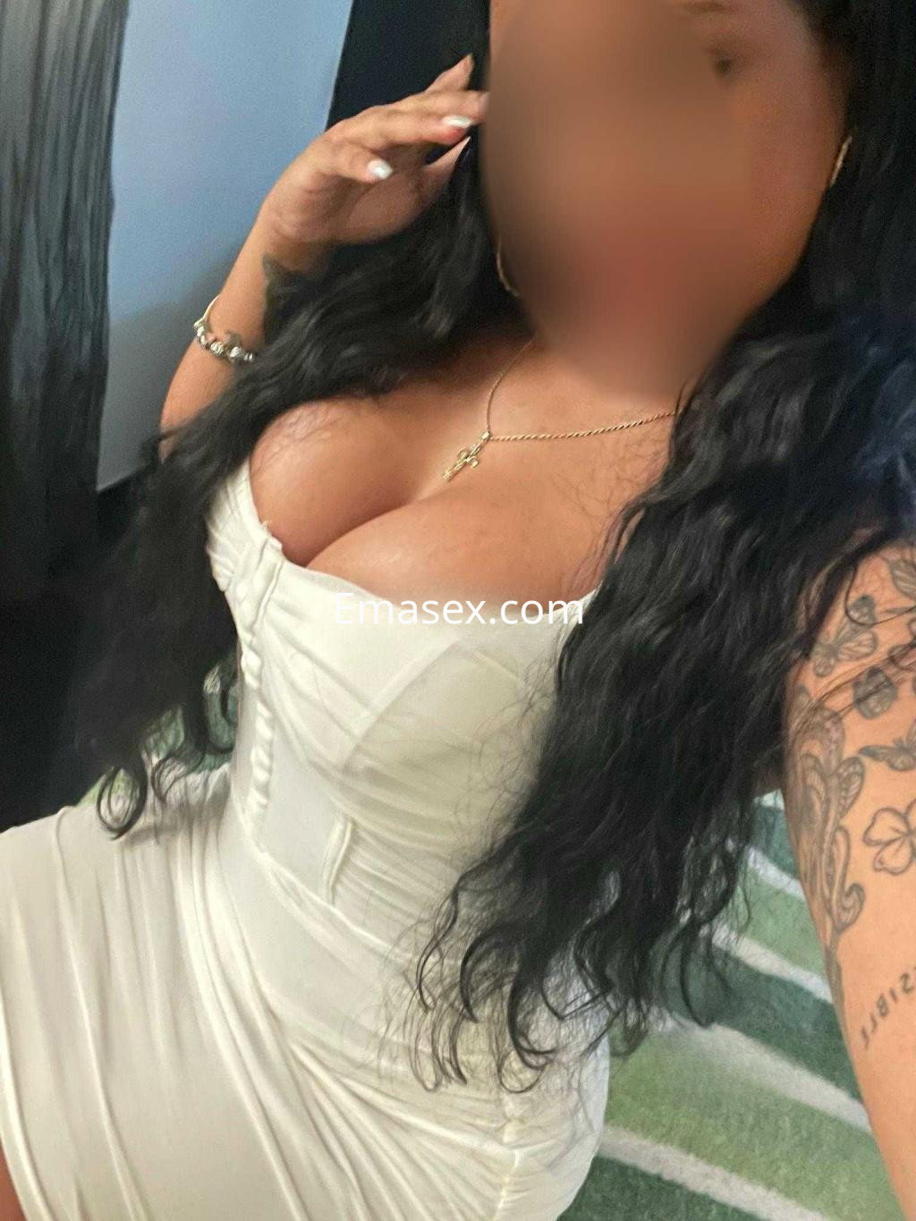 Escort en Castellón con vestido ajustado blanco, cabello largo y ondulado, posando en un ambiente interior.
