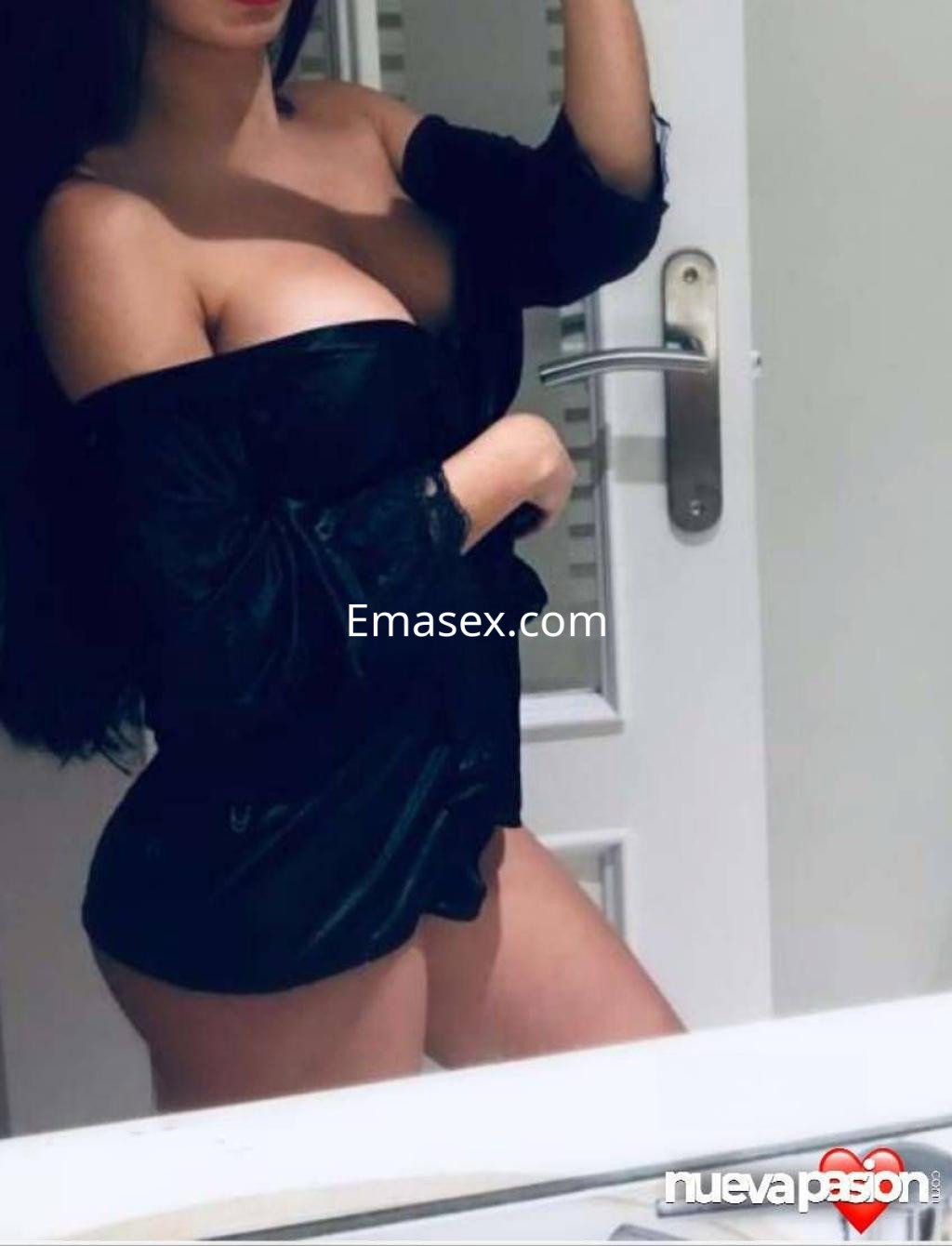 Puta posando con una blusa negra ajustada en un ambiente interior de Sevilla, mostrando su figura y cabello largo.