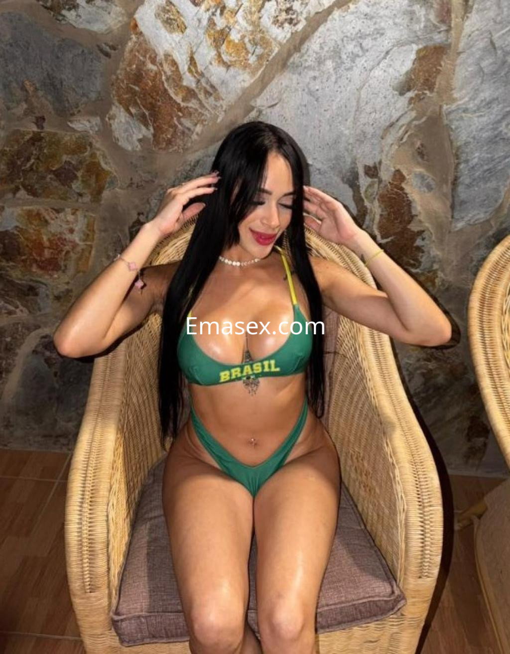 Escort en Las Palmas sentada en una silla de mimbre, vistiendo un bikini verde con el logo de Brasil, con cabello largo y lacio.