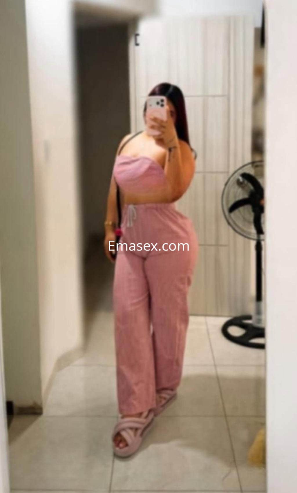 La escort en Albacete se muestra frente a un espejo, vistiendo un conjunto rosa sin mangas y pantalones largos.