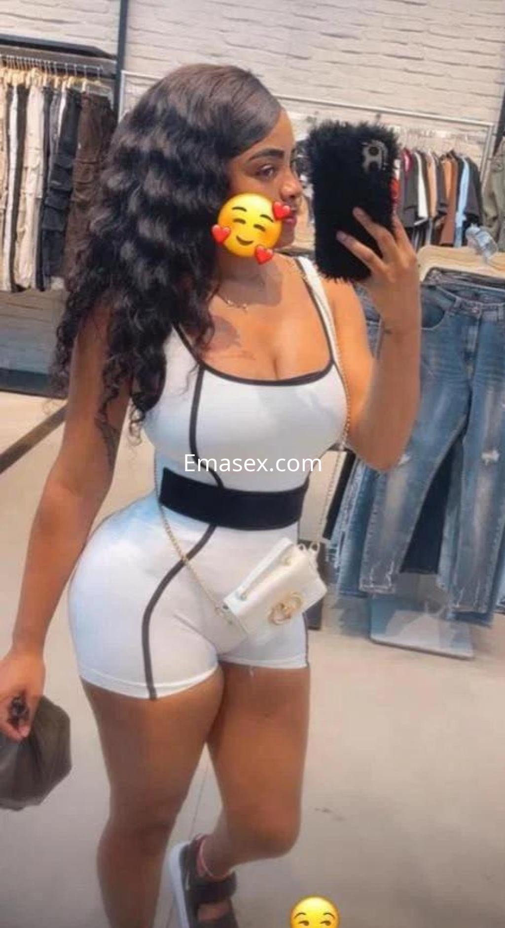Escort en Albacete con cabello ondulado y largo, viste un conjunto blanco ajustado y se toma una selfie en una tienda.