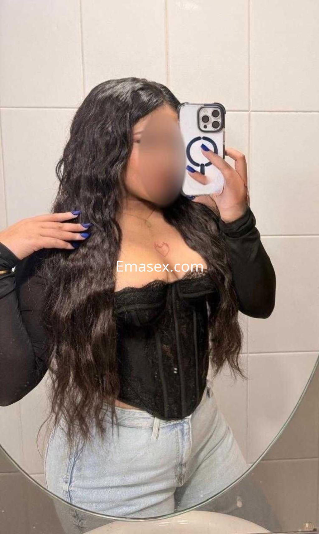 Escort en Almería se fotografía en el espejo, vistiendo un corset negro y jeans claros, con cabello largo y ondulado.