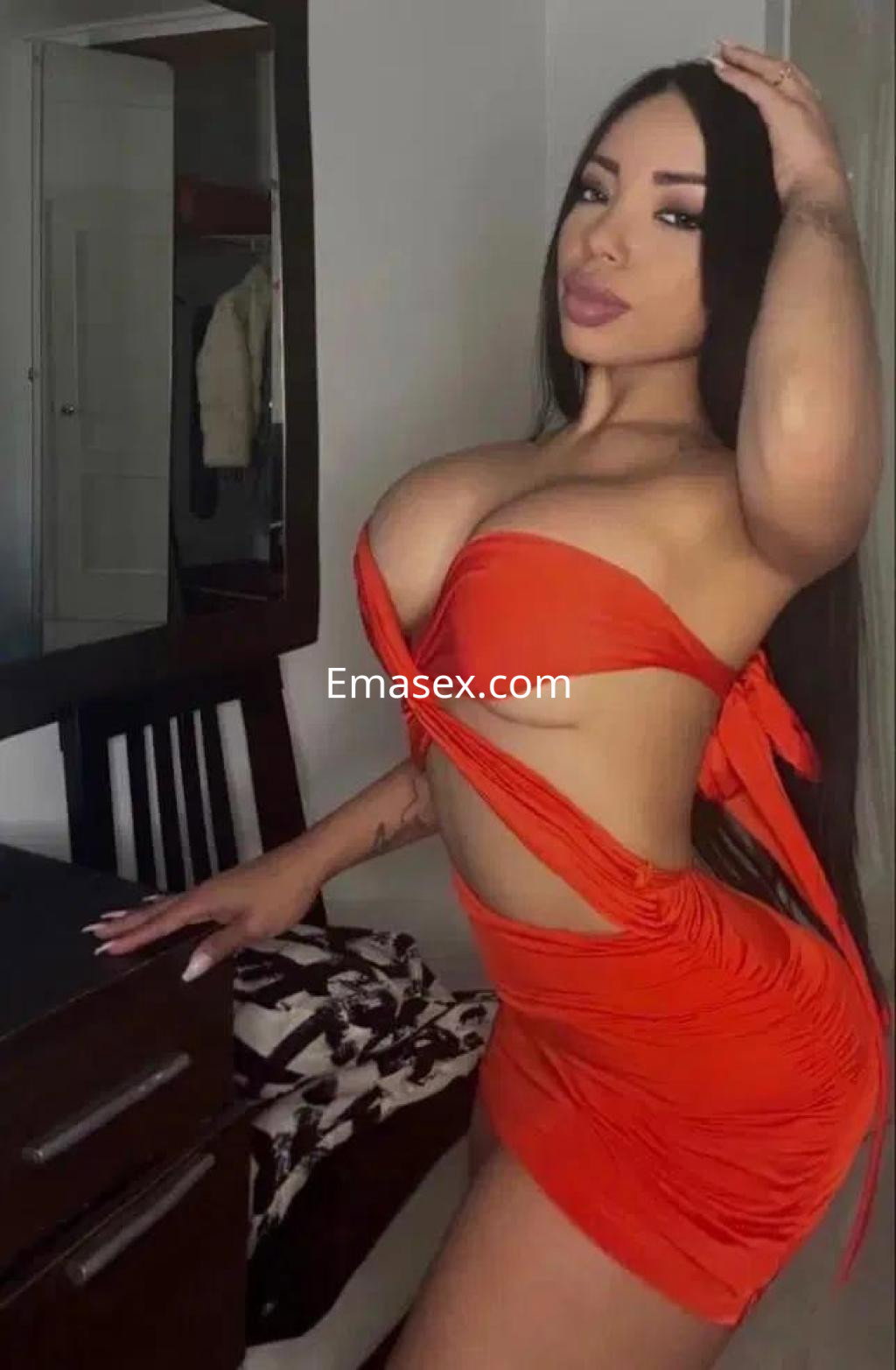 Puta posando con un vestido rojo ajustado y escotado, en un ambiente interior de Almería.