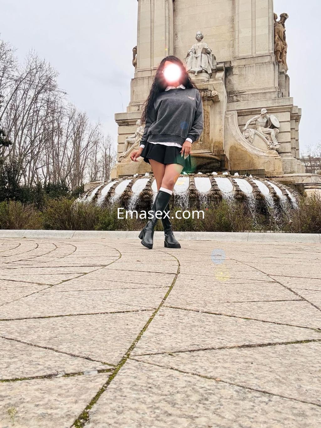 Escort en Logroño, con un atuendo casual que incluye un suéter y una falda corta, posando en un parque.