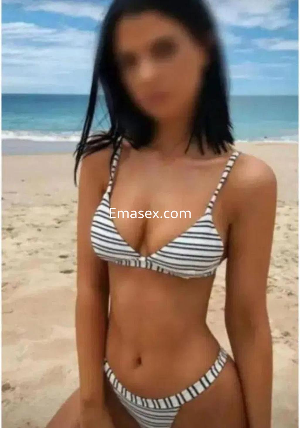 Escort en Castellón luciendo un bikini de rayas en la playa, con el mar de fondo y cabello oscuro.
