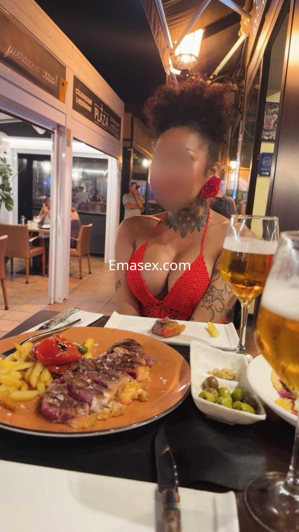 La puta en Almería se muestra en un restaurante, luciendo un top rojo, con cabello rizado y un plato de comida.