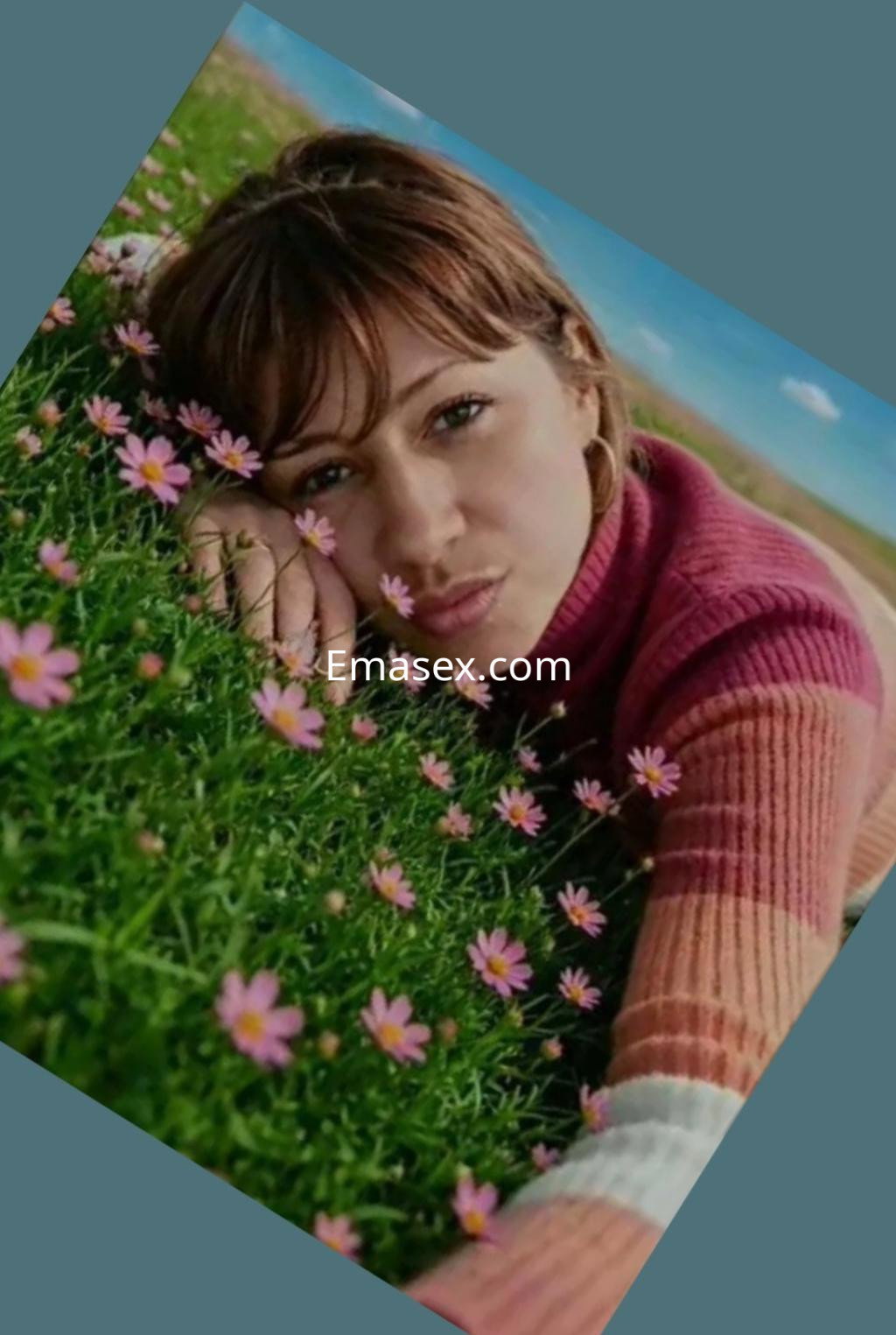 La puta posa en un campo de flores en Vigo, vistiendo un suéter de rayas y con el cabello suelto.