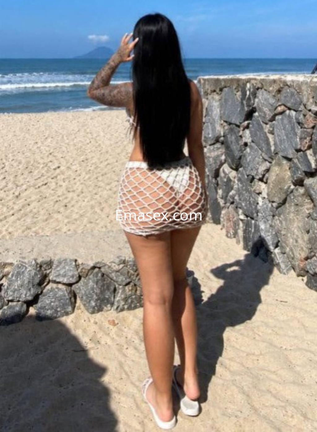 Puta en Gijón, con cabello largo y lacio, vistiendo una falda de red, de espaldas frente al mar.