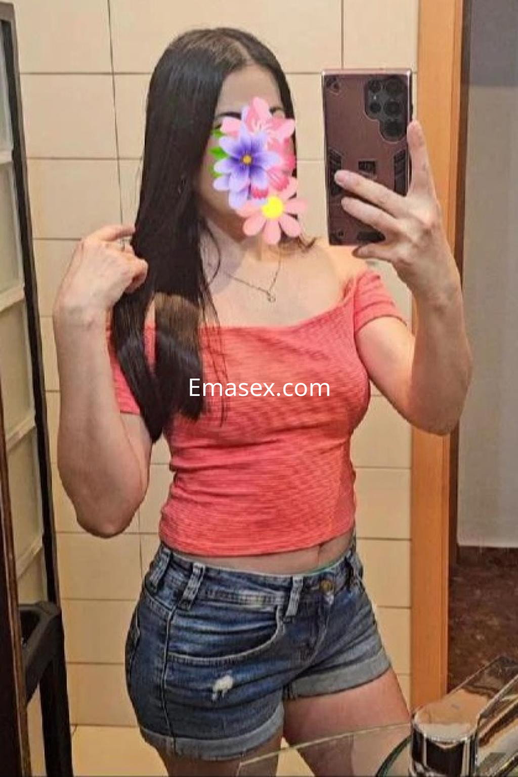 Escort en Córdoba posando en un espejo con blusa rosa y shorts de mezclilla, mostrando su cabello largo.