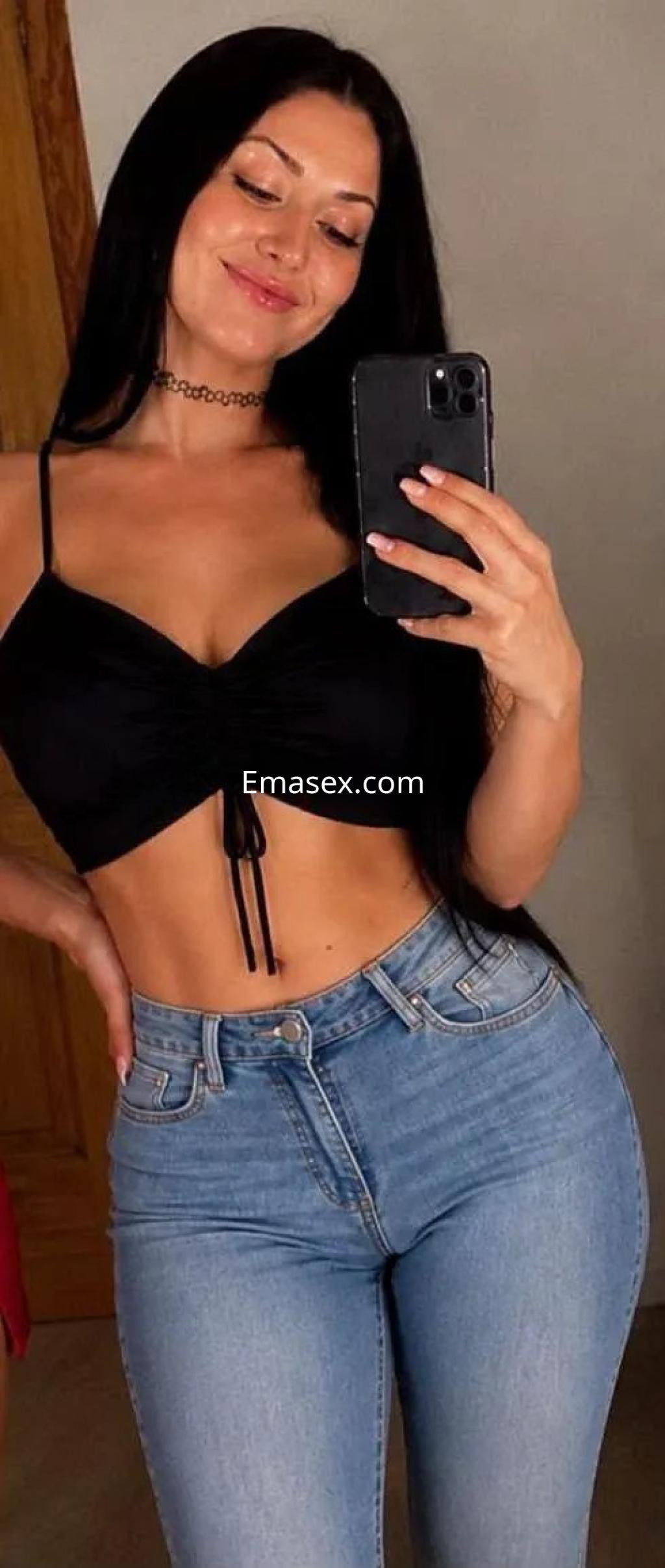 Puta en Córdoba luciendo un top negro ajustado y jeans claros, sonriendo mientras toma una selfie.
