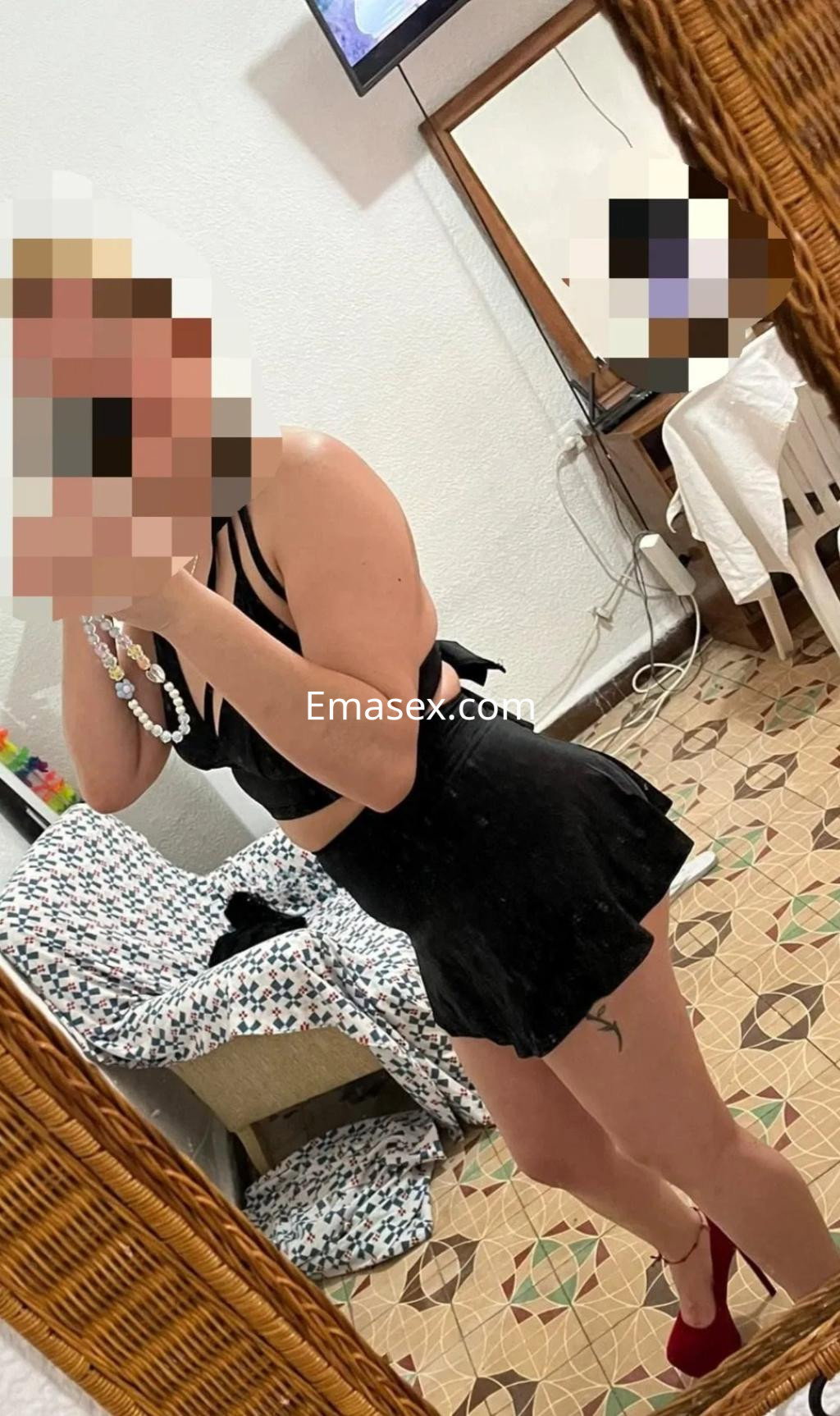 Puta en Albacete muestra un conjunto negro de dos piezas y tacones rojos, reflejándose en un espejo.