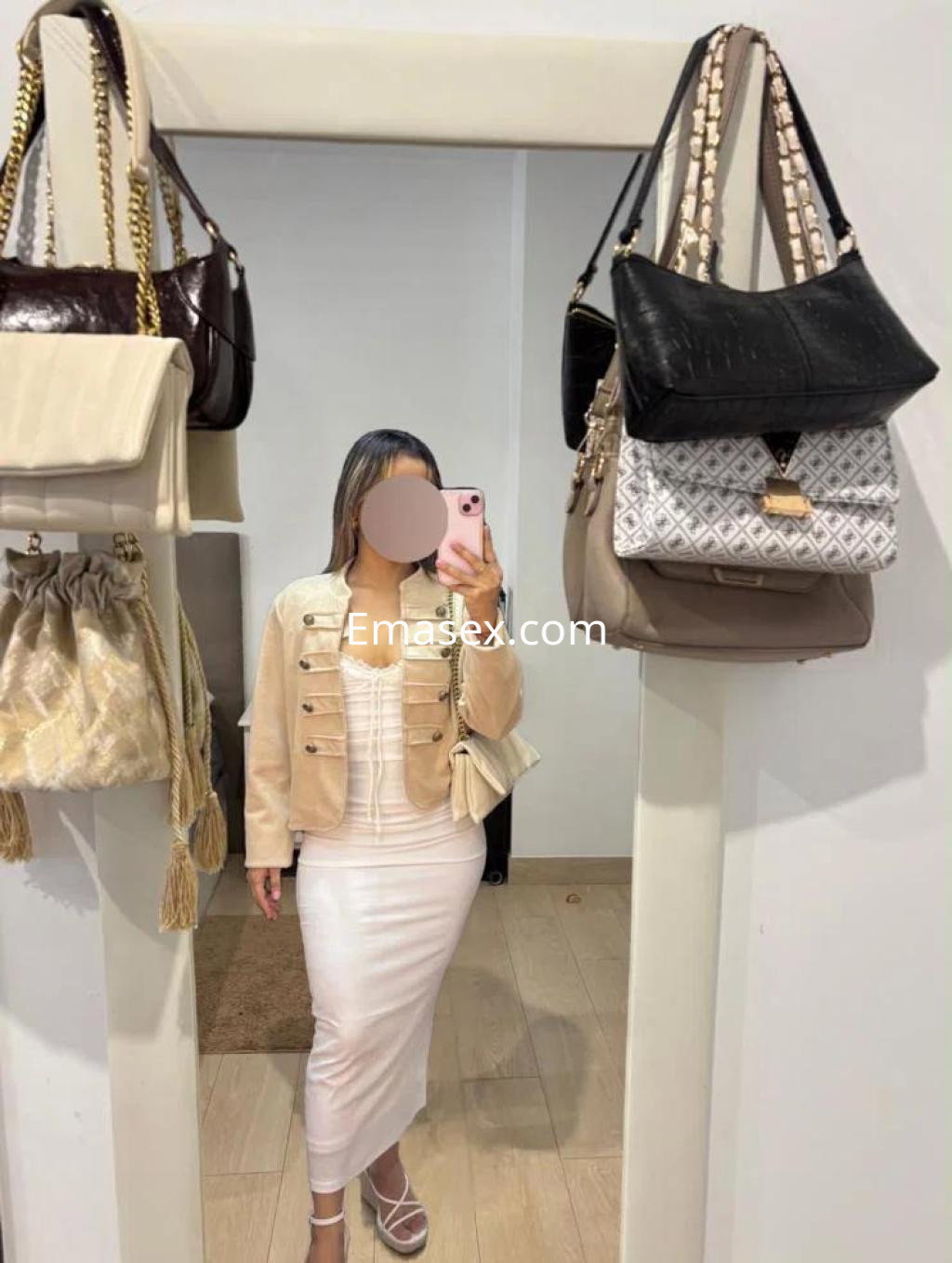 Escort en Almería con cabello largo y lacio, viste un vestido blanco y una chaqueta clara, posando frente a un espejo.