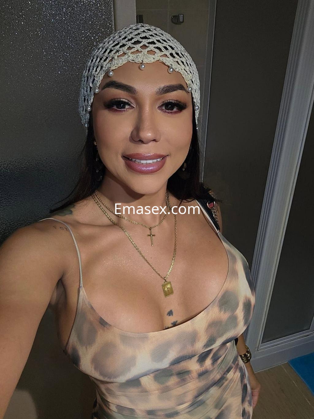 Puta trans en Pamplona, con un vestido de estampado animal y tocado de red, sonríe frente al espejo.