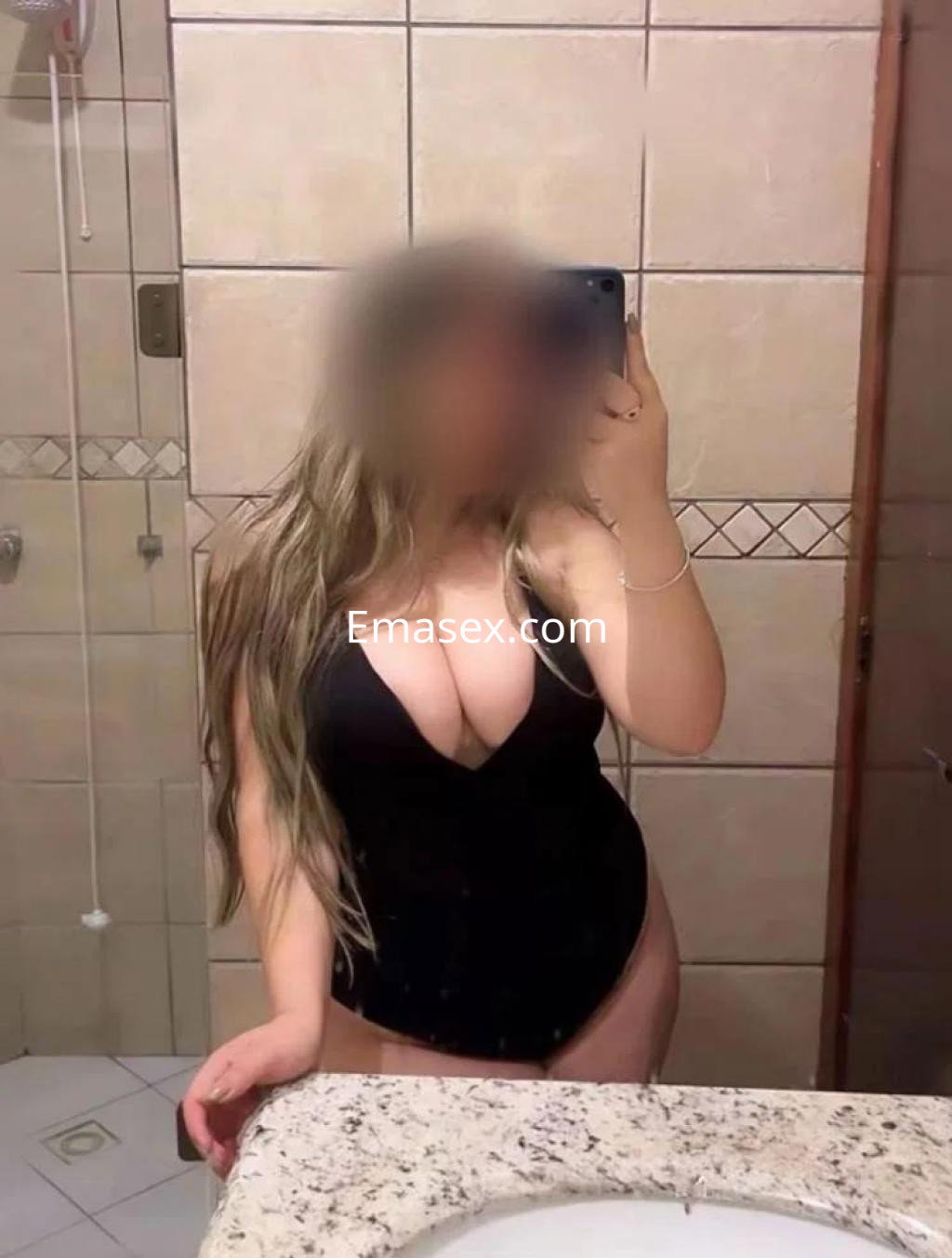 Puta en Badajoz, luciendo un traje de baño negro con escote pronunciado, posando en un baño.