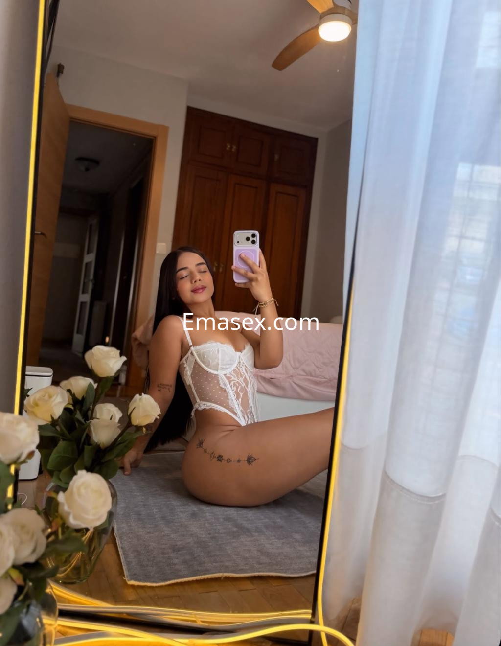 Puta en Pamplona con cabello largo y lacio, vistiendo un body blanco con transparencias, posando en un espejo.