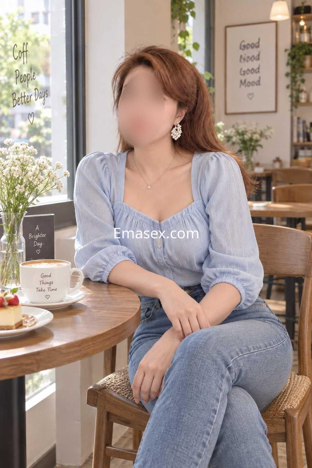 Puta sentada en una cafetería de Granada, con blusa azul y jeans, luciendo un estilo casual y elegante.