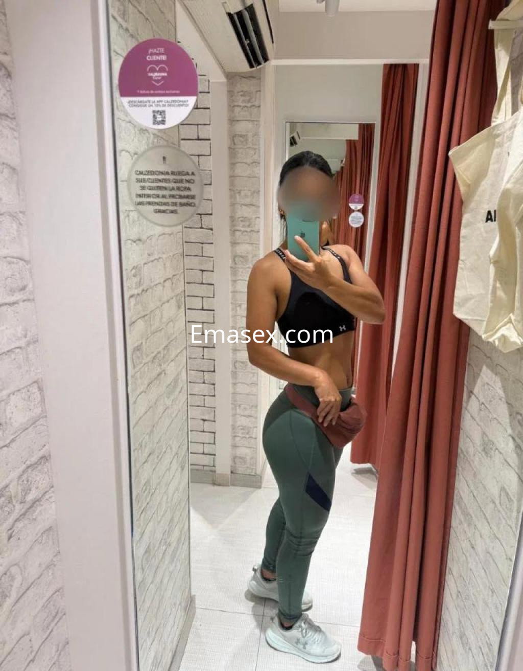 Puta en Palma de Mallorca se mira en el espejo, vistiendo un sujetador negro y leggings verdes ajustados.