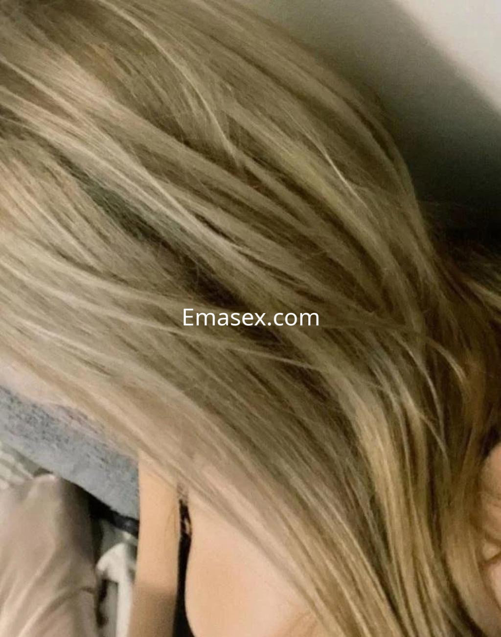 Escort en Castellón con cabello largo y rubio, recostada sobre una superficie suave y con un fondo desenfocado.