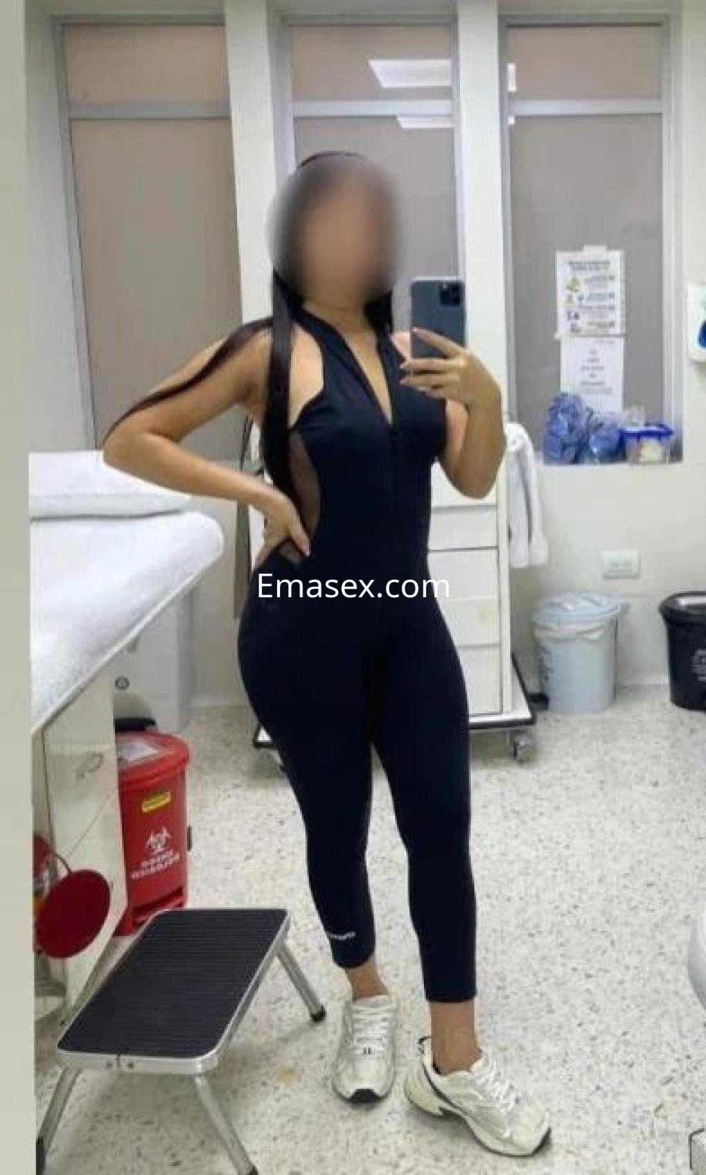 Escort en Las Palmas posando en un espejo con un conjunto deportivo negro y zapatillas blancas en un ambiente interior.