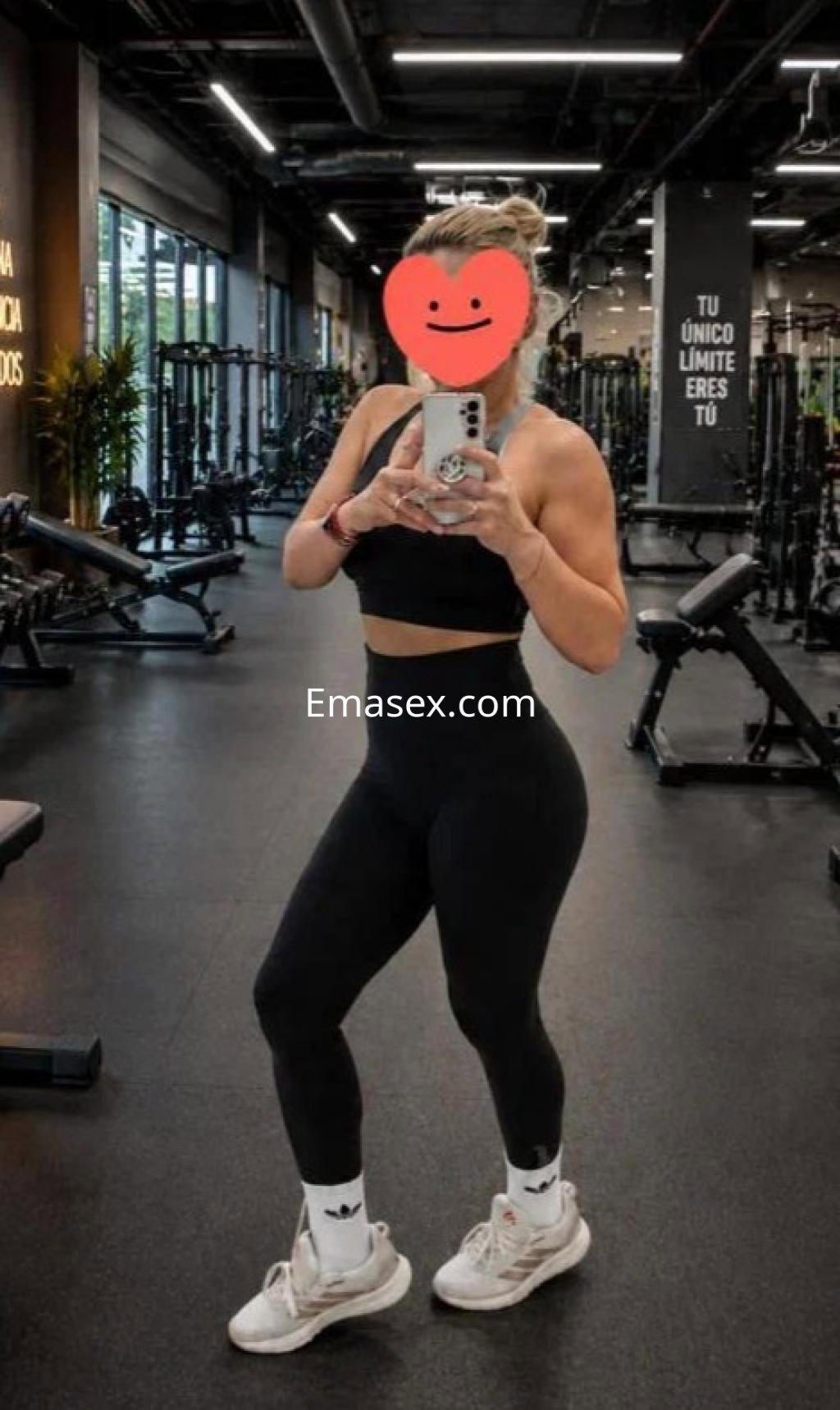 Puta en Las Palmas, con cabello recogido y rubio, viste top negro y leggings ajustados, posando en un gimnasio.