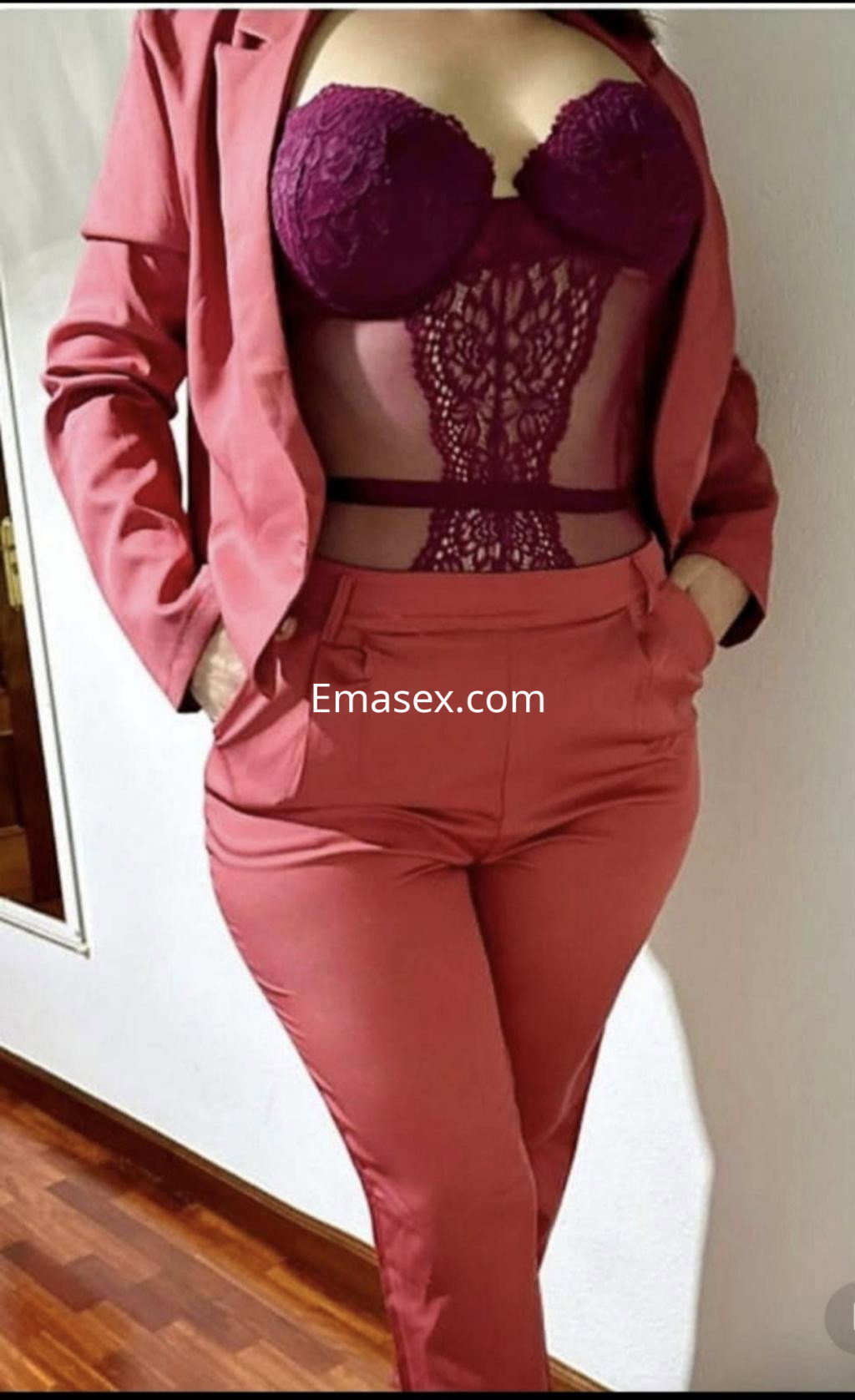 Puta en Donosti viste un conjunto de sastre rosa con una blusa de encaje morado, mostrando confianza en un ambiente interior.