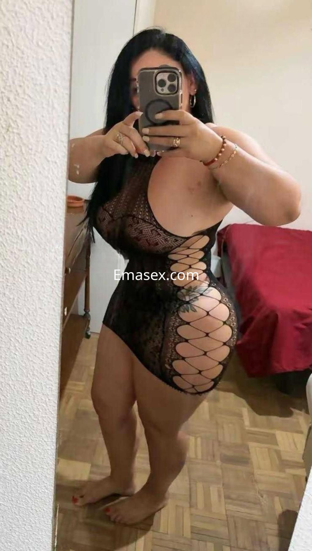 Escort en Badajoz luciendo un vestido de lencería negro con detalles en los costados, posando frente a un espejo.