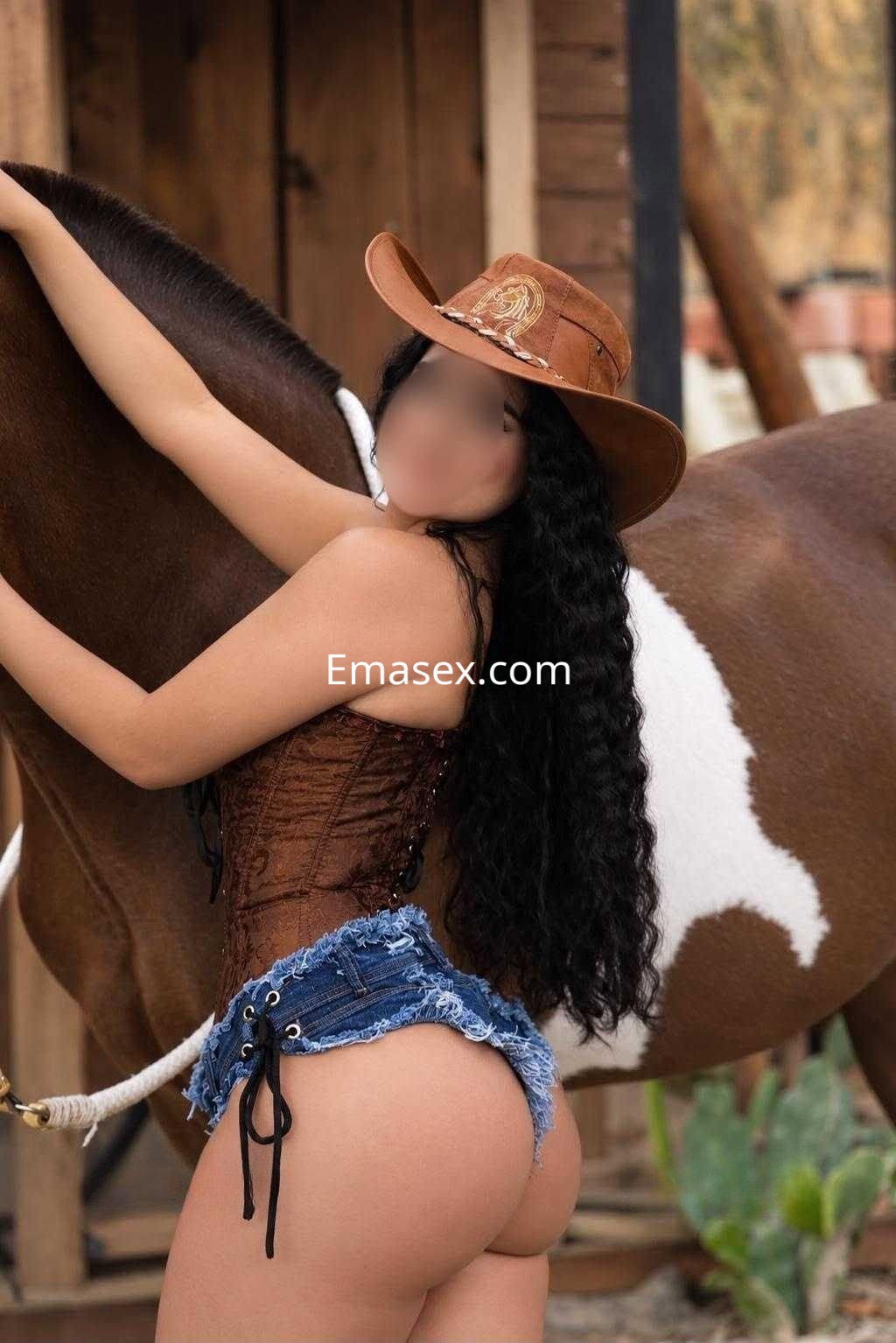 Puta posando junto a un caballo, vistiendo un corsé marrón y shorts de mezclilla en Granada.