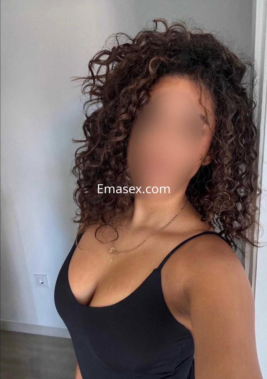 Escort en Albacete con cabello rizado y suelto, luciendo un top negro, en un entorno interior luminoso.