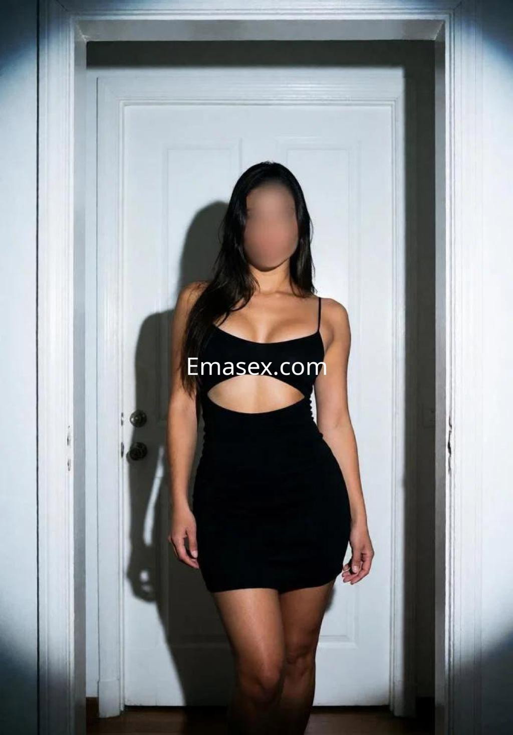 Puta posando en un vestido negro ajustado con un corte en la cintura, en un interior con puerta blanca en Cáceres.