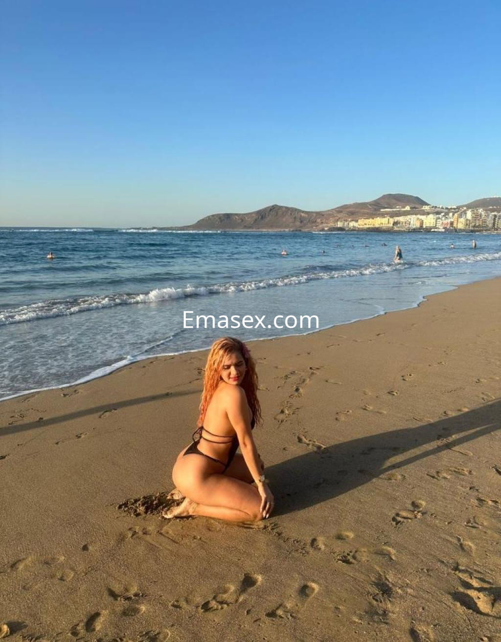 La escort posa en la playa de Las Palmas, luciendo un bikini negro y con el mar de fondo.