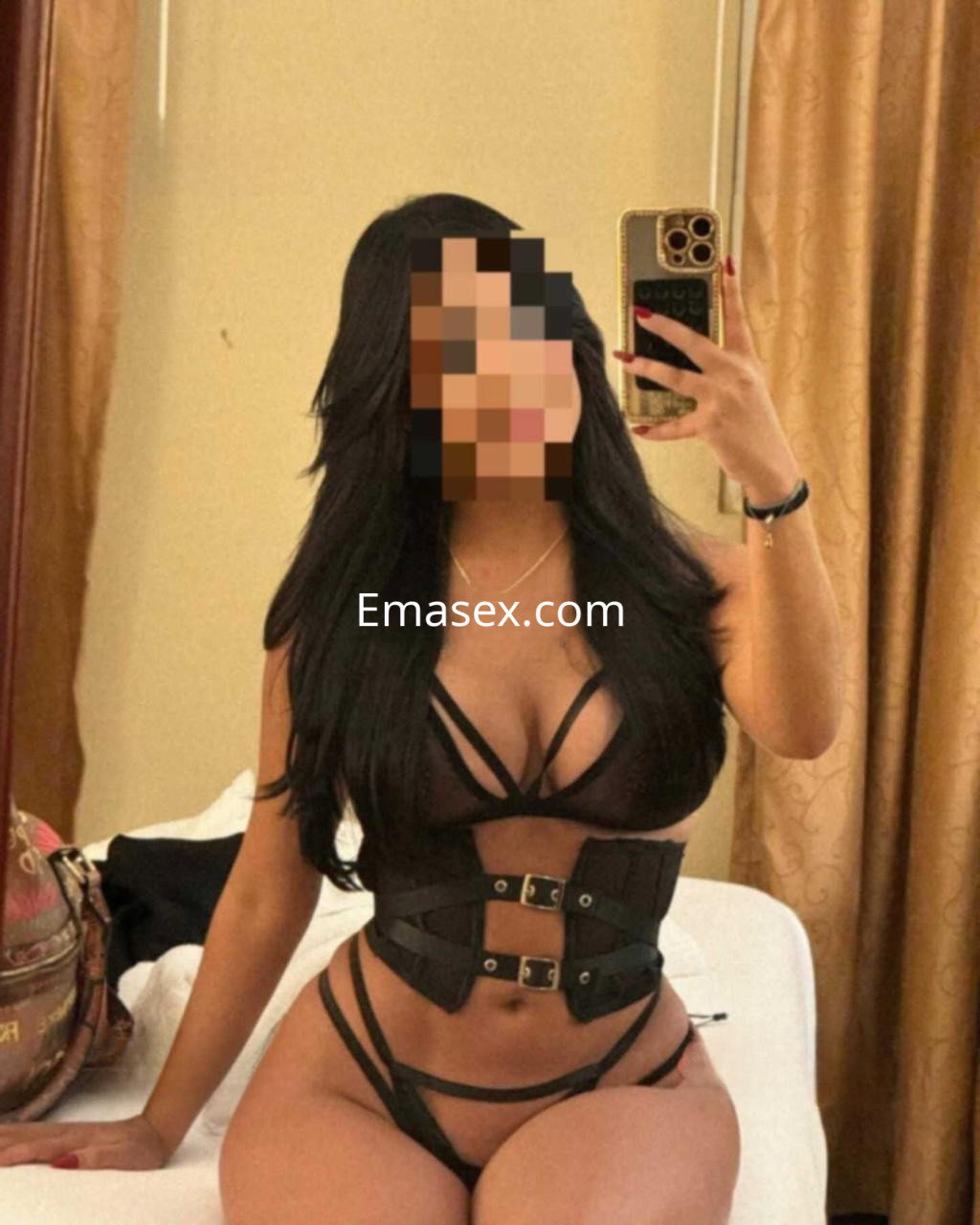 Escort en Badajoz posando en un espejo, vistiendo un conjunto de lencería negra con corset y tirantes.
