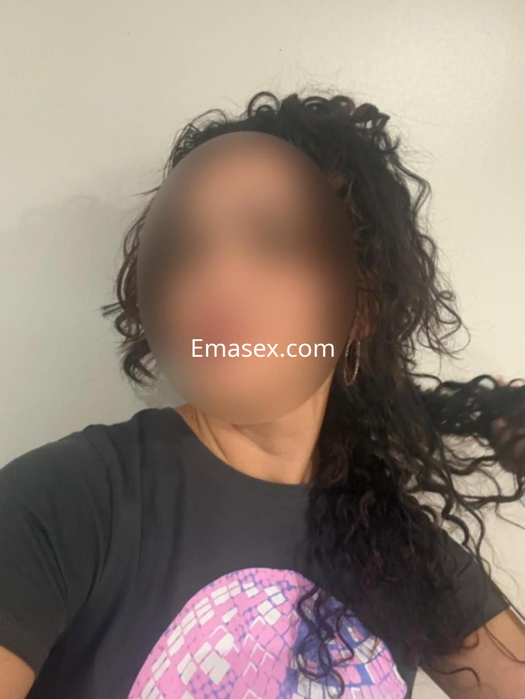 Puta con pelo rizado y suelto, viste una camiseta negra en un fondo neutro, posando de perfil en Bilbao.